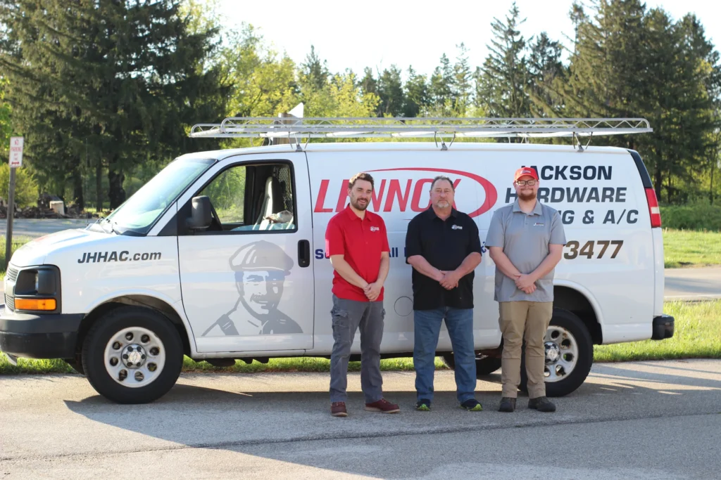 Three people stand in front of a service van with company branding in a sunny outdoor setting, surrounded by greenery.